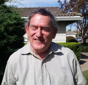 Outdoor photo of an elder white man wearing a collared shirt, smiling.
