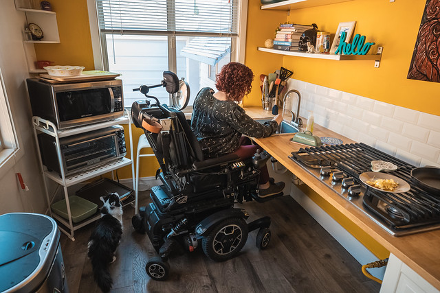 Photo of a woman in a wheelchair washing dishes in a sink that she is able to roll under.