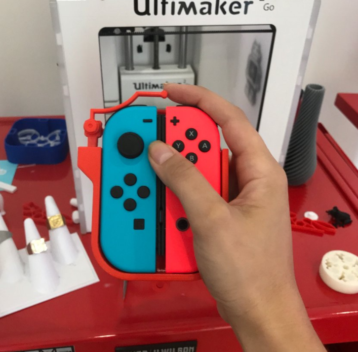 A hand holding a pair of Joy-Cons joined together by a 3D printed one-handed casing.