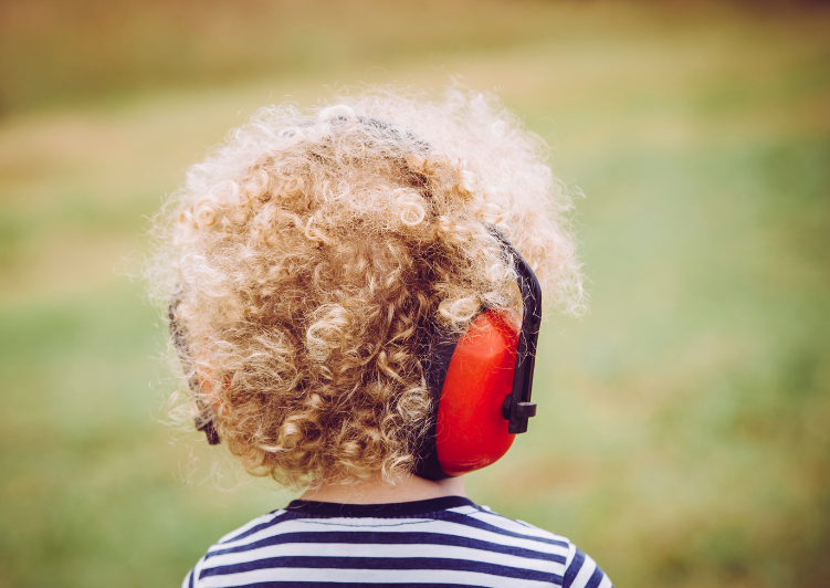 A behind shot of a small child with curly blond hair wearing noise cancelling headphones.
