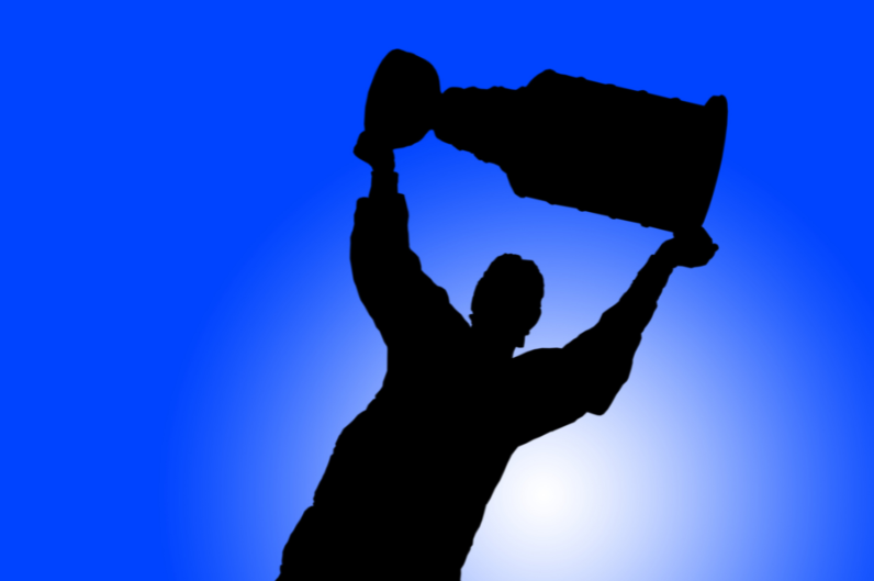A silhouette of a person hoisting the Stanley cup above their head. 