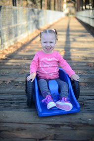 Photo of a smiling toddler on a plastic wheelchair.